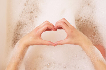 Fototapeta premium woman making heart shape with hands over bath foam