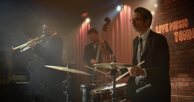 Portrait of a Male Drummer in Glasses Playing Live Jazz Music on Stage at a Bar Concert Event, Driving the Band&rsquo;s Song as Trumpet and Bass Perform for the Audience in a Smoky Club.
