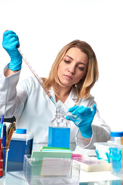 Young european female scientist using serological pipette transferring blue reagent in lab