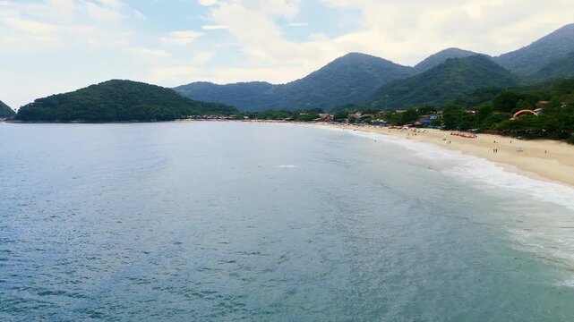 Aerial view of Trindade Beach with tourists, umbrellas and turquoise ocean water from sea perspective in Paraty, Brazil. Push in diagonal camera movement