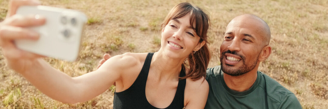 Multi-ethnic athletes, beautiful fit girl and strong man take a picture of themselves. Happy woman taking selfies with boyfriend. Panoramic. Panoramic