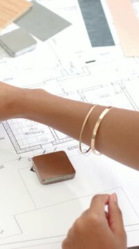 Vertical video: Starting on plan, hand with bracelets sliding wood plank at desk, choosing finishes
