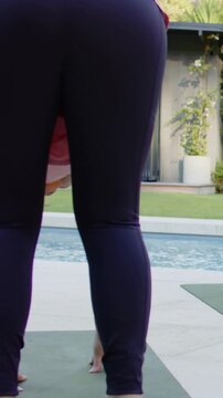 Vertical video: Starting bent woman in leggings pink top folding on green mat on deck for exercise