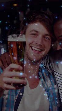 Vertical video: After clink man in blue plaid raising beer, smiling, sparkles marking toast at bar