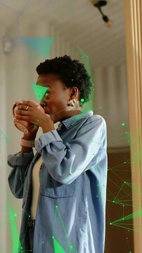 Vertical video: Adult woman lifting pink mug and sipping, then calling as green tech shapes growing
