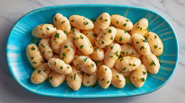 Overhead-view of authentic Italian Gnocchi di patate, traditional Italian potato dumplings made from boiled floury potatoes. Paired with sage butter. On a blue ceramic plate, marble surface. 