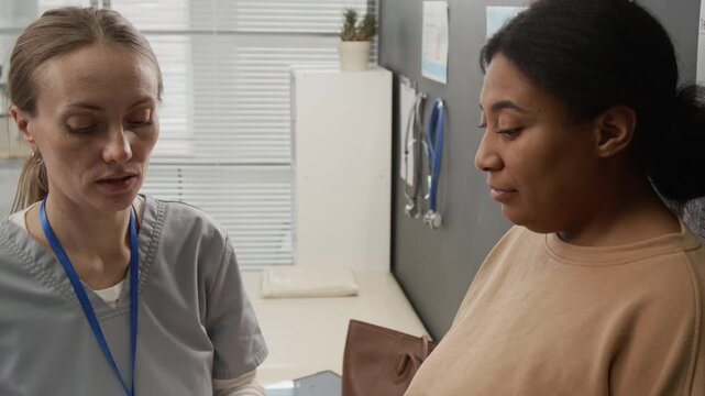 Positive Caucasian female doctor measuring height of Black woman and taking notes during appointment in reproductive center