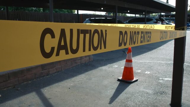 Yellow caution tape do not enter blocking parking area with cone daytime showing restricted access safety control and temporary closure of outdoor space
