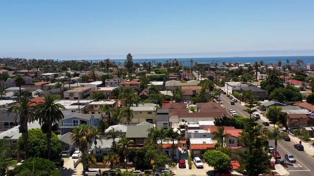 Drone rising above homes and palm trees in Ocean Beach San Diego moving toward the coastline and ocean.