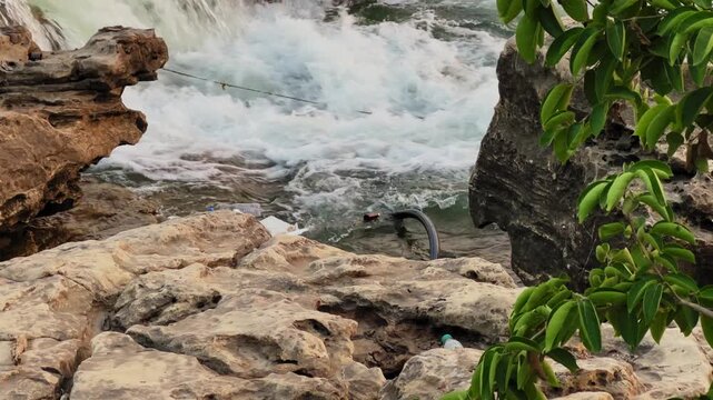 Close view of river water flowing over rocks with visible floating garbage and debris, highlighting pollution and environmental impact in a natural outdoor setting