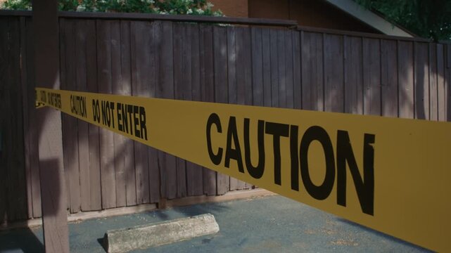Yellow caution tape do not enter stretched along fenced restricted zone daytime showing restricted access safety control and perimeter monitoring in outdoor environment
