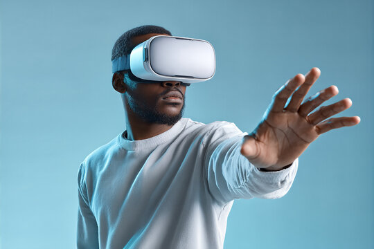 African American VR user in a light gray sweatshirt wearing a white headset reaches forward with focused expression against cool blue backdrop