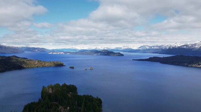 Static afternoon aerial timelapse over Nahuel Huapi lake. Fast-moving stratocumulus clouds project dynamic shadows over the lake and Andes mountains, with changing water textures in Patagonia.