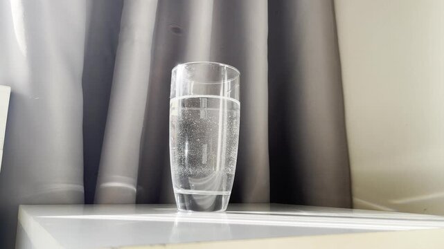 refreshing sparkling water glass resting on bedside table near tufted headboard in bright sunlight