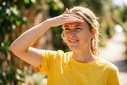 Young woman shielding eyes from bright sun outdoors