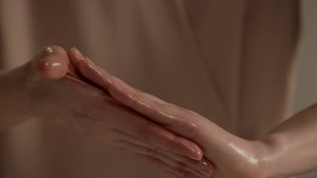 Close up of unrecognizable female therapist rubbing hands together with massage oil before session, preparing for body treatment in calm wellness environment