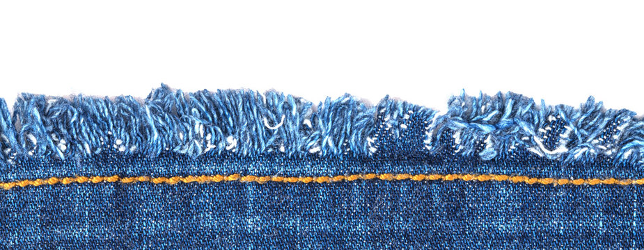 Frayed edge of denim fabric shows blue threads and seam with yellow stitching during daylight