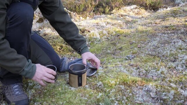 Hiker packing camp meal with portable cookware on mossy forest ground
