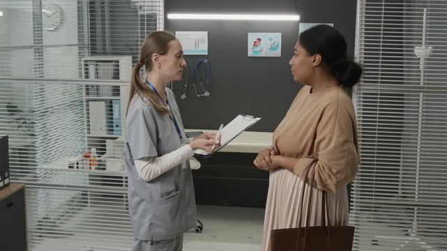 Female doctor explaining medical service contract to client and asking her to sign it after appointment in fertility clinic
