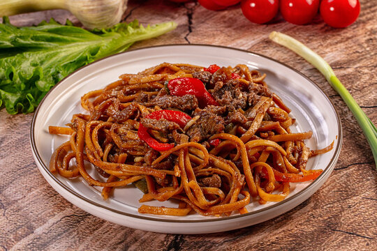Asian beef noodle stir fry with red peppers on a plate. Close up of a hearty meal with fresh vegetables on a rustic wooden table