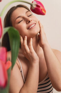 A portrait of an attractive young woman surrounded by tulips near her face. Femininity, the concept of nature's awakening, the scent of flowers, tenderness, and grace. vertical photo