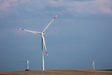 Fototapeta premium White wind turbines operating on a dry hill against a blue sky