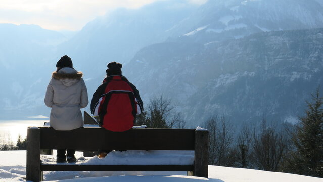 A couple enjoys a scenic view of snow-covered mountains and a lake.