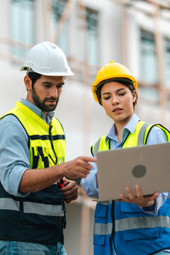 Construction worker team with hard hat and safety vest review plan on laptop at building site