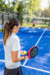 Naklejka premium Woman holding padel racket and ball preparing to serve on outdoor court, calm moment before next rally in doubles match.