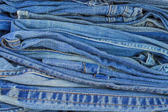 Faded blue denim jeans stacked in a pile at a textile recycling center in the afternoon sun