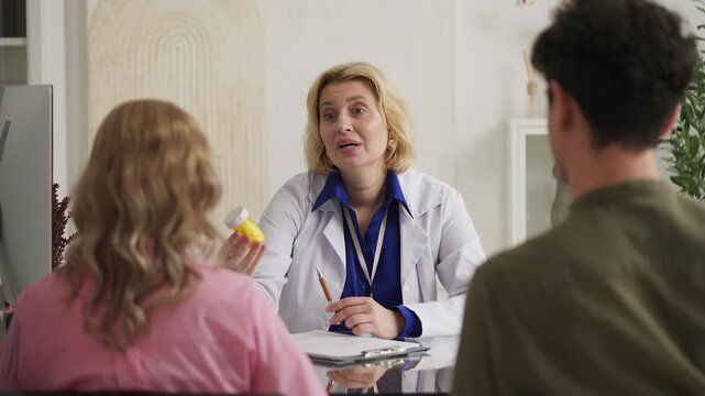 Friendly woman gynecologist prescribing pills to young couple, health check-up