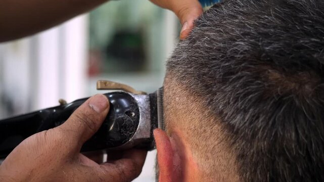 Barber uses electric clipper to cut a young mans hair. The scene highlights precision, speed, and modern fade haircut technique in a professional barbershop.