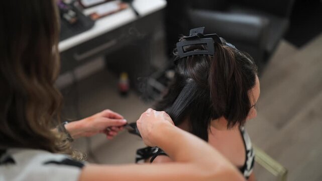 Stylist's steaming flat iron straightens young woman's brunette hair