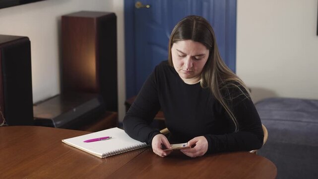 Young woman sits at a table counting cash and feeling financial stress, a relatable scene for bills, debt, budgeting, and money problems.