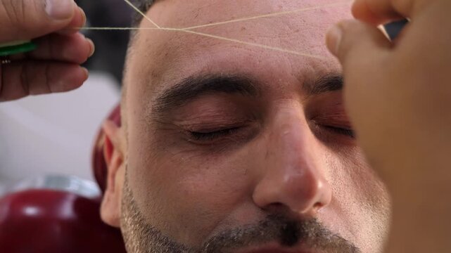 Close-up of eyebrow threading on a young man. The scene captures fine detail, precision, and control in modern facial grooming techniques