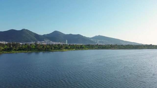 Serene lake landscape with distant mountains and lush green trees under a clear sky