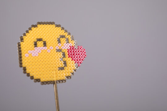 Handmade perler bead emoji blowing a kiss against a soft gray background.