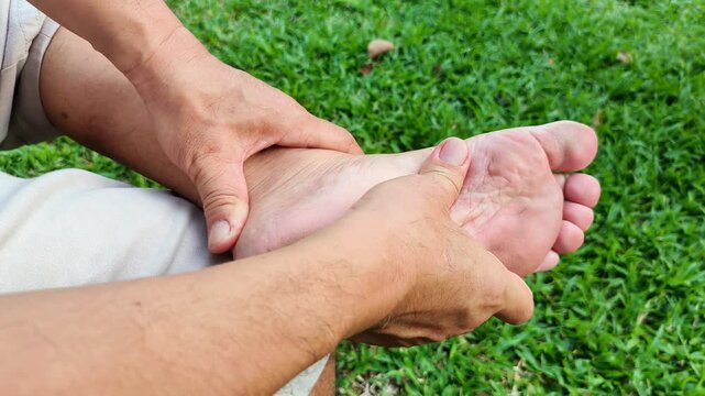 Man experiences pain in his bare feet while sitting on a park bench. Foot pain due to plantar fasciitis and prolonged standing. Health and medical concepts.