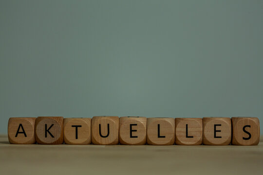 Wooden cubes with letters spell Aktuelles, meaning current or latest news. Concept of information fl