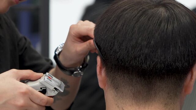 Barber using electric hair clipper to trim back of a man head