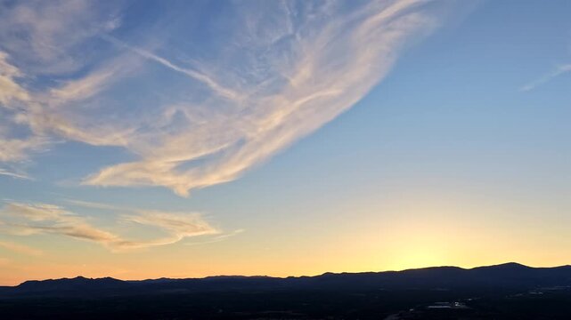 This cinematic drone hyperlapse captures a sunburst disappearing over a mountain horizon. Swift wispy clouds and sunset light create an epic and universal backdrop.