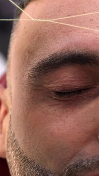 Vertical: Close-up of eyebrow threading on a young man. The scene highlights control, fine detail, and professional grooming technique.