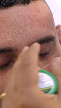 Vertical: Barber shapes eyebrows using thread on a young man. The scene emphasizes precision, symmetry, and attention to detail in facial grooming.