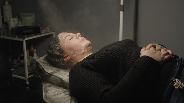 Woman lying on a couch during facial steaming procedure in clinic