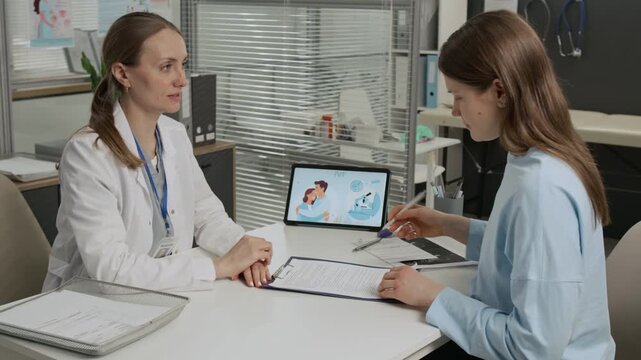 Medical specialist asking gen Z client to sign medical service contract and shaking hands with her during fertility consultation