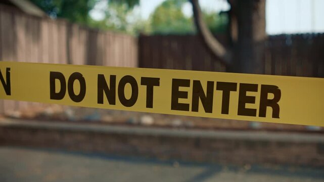 Yellow caution tape do not enter close up against blurred restricted area daytime shows restricted access area safety and perimeter control in outdoor environment
