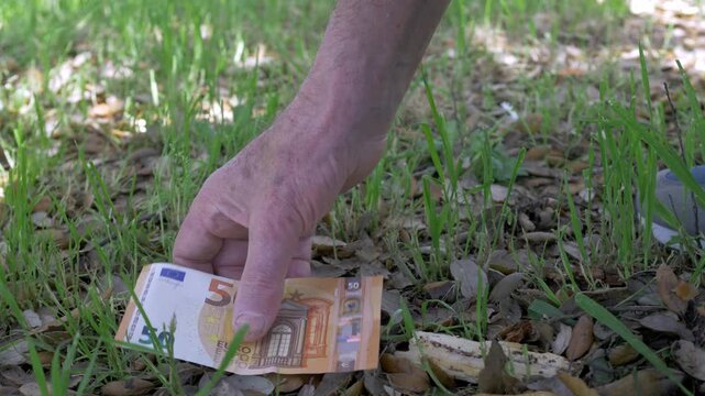 Close-up of an elderly hand picking up a 50 euro banknote from grass, representing chance, discovery, and the unexpected recovery of lost money outdoors.