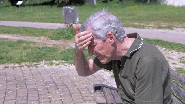 Elderly man wiping sweat from his forehead in a park under intense summer heat, showing exhaustion, discomfort, and the impact of high temperatures.