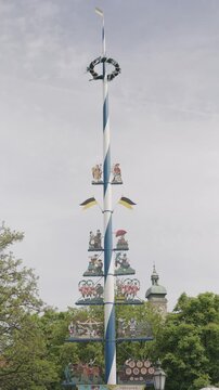 Decorated bavarian maypole standing tall against a cloudy sky with trees in the background Oktoberfest