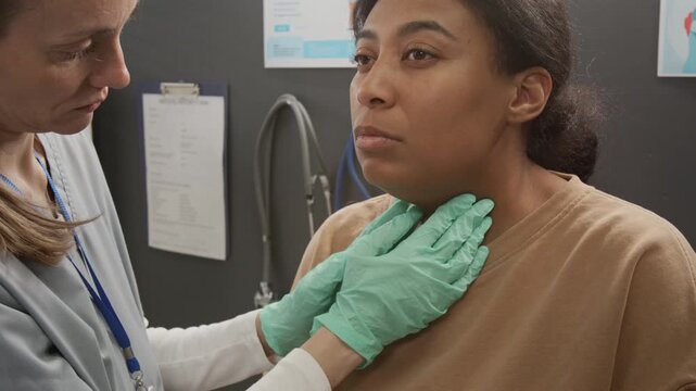Female endocrinologist wearing medical gloves examining neck of young woman during clinical consultation